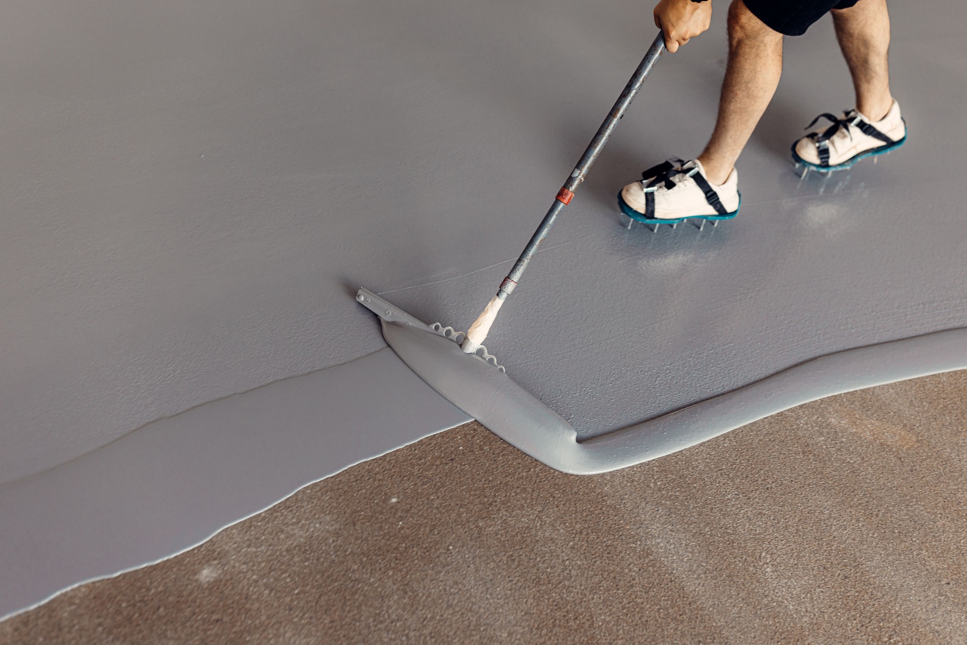 Construction worker applying grey epoxy resin in an industrial hall